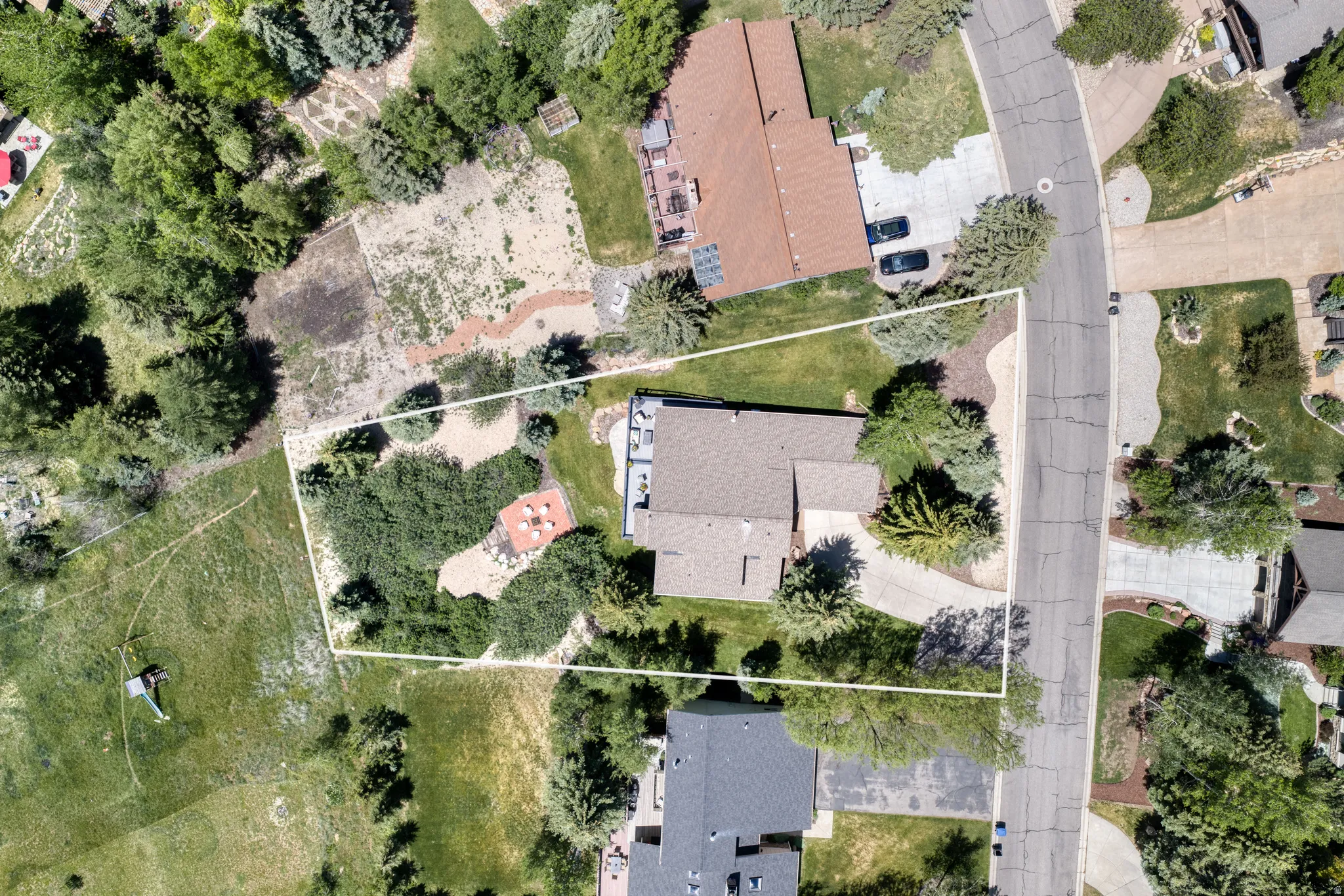 Expansive property showcasing a single-story residence with a brown shingle roof, a paved driveway, and mature landscaping