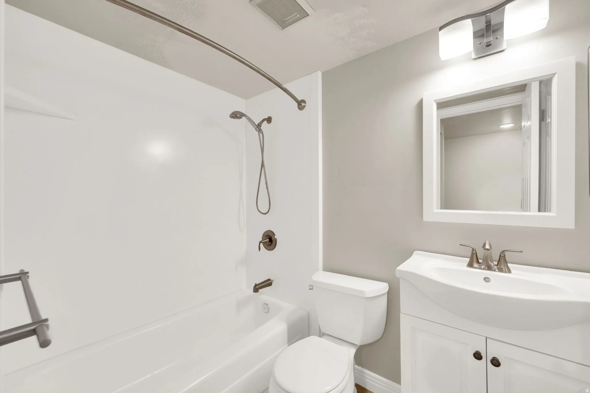Bathroom featuring a white tub/shower combination, bronze-finish fixtures, white vanity with integrated sink, white framed mirror, and chrome-finish light fixture