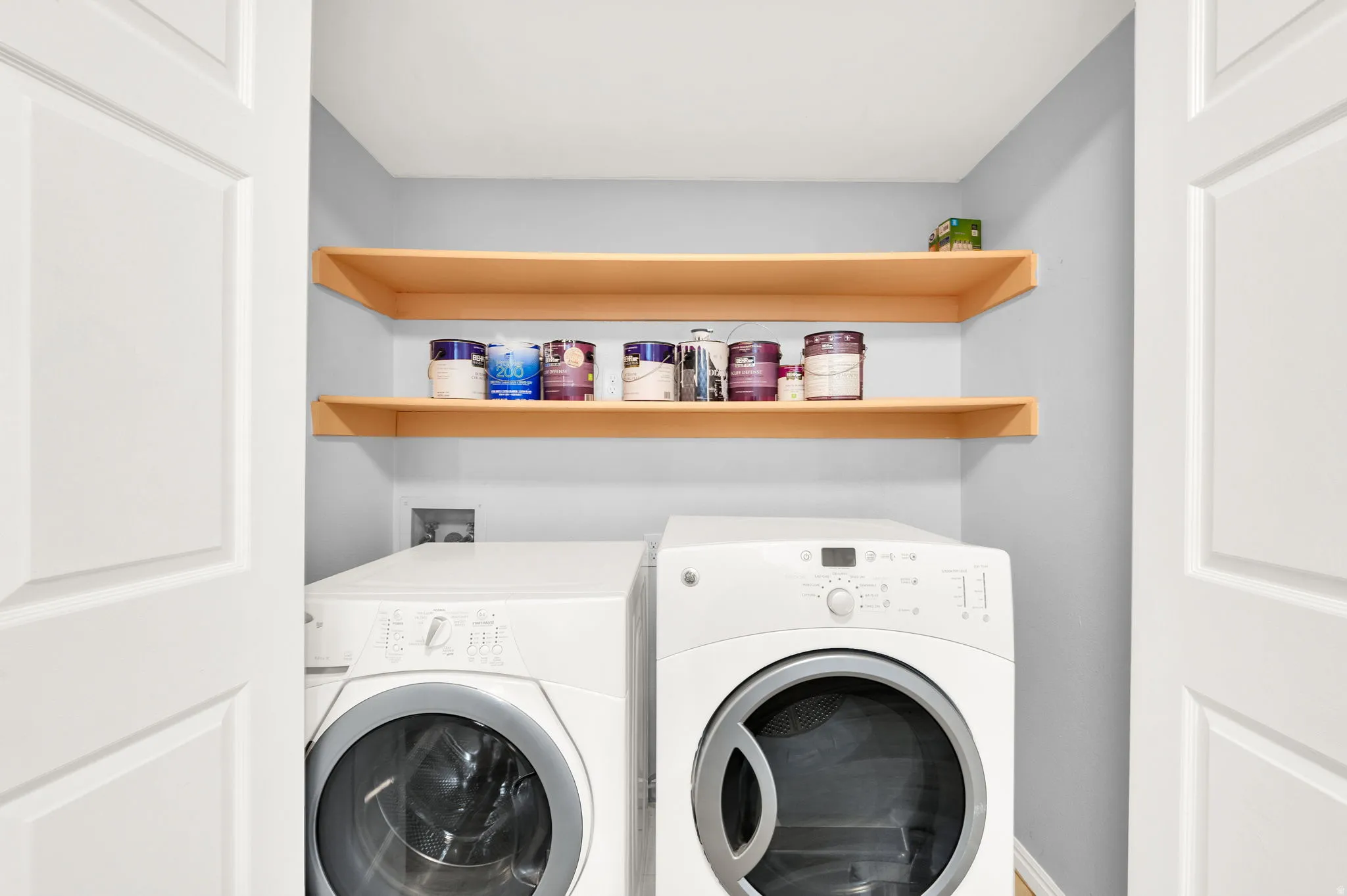 Dedicated laundry space featuring a stackable washer and dryer, light wood-finish shelving, and panel doors