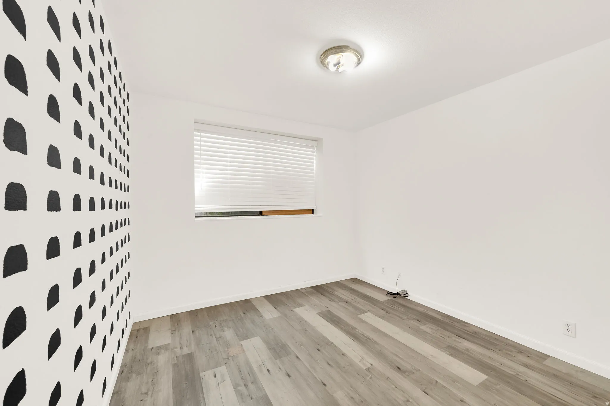 Room featuring a patterned accent wall, light wood-finish flooring, and a single window with horizontal blinds