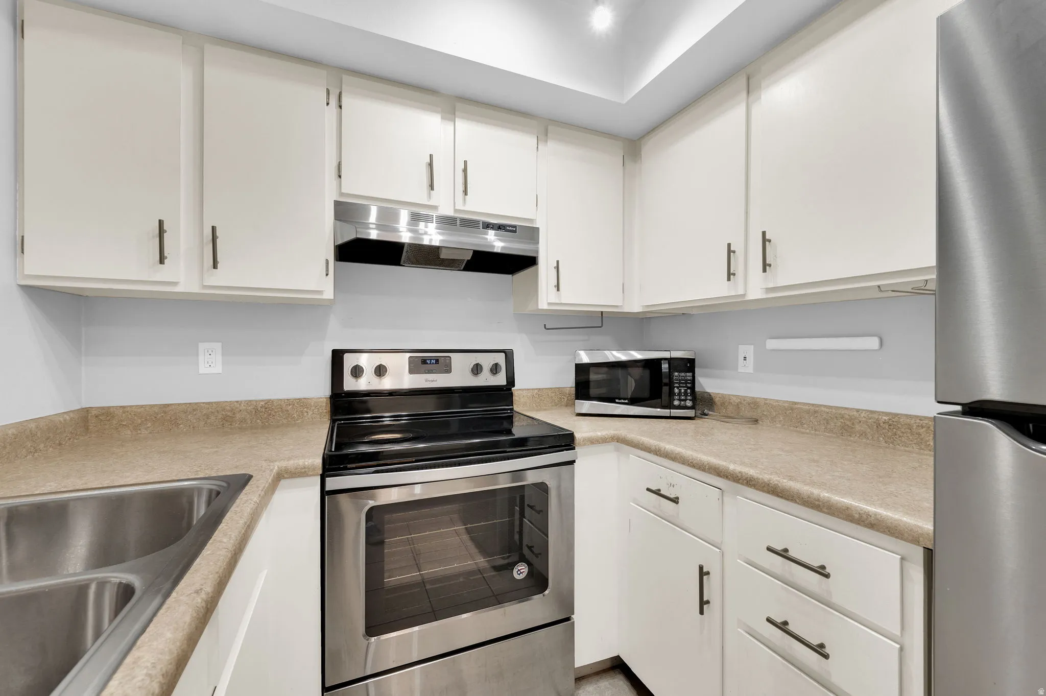 Kitchen featuring white cabinetry, light-toned countertops, a stainless steel electric range, and a double basin stainless steel sink
