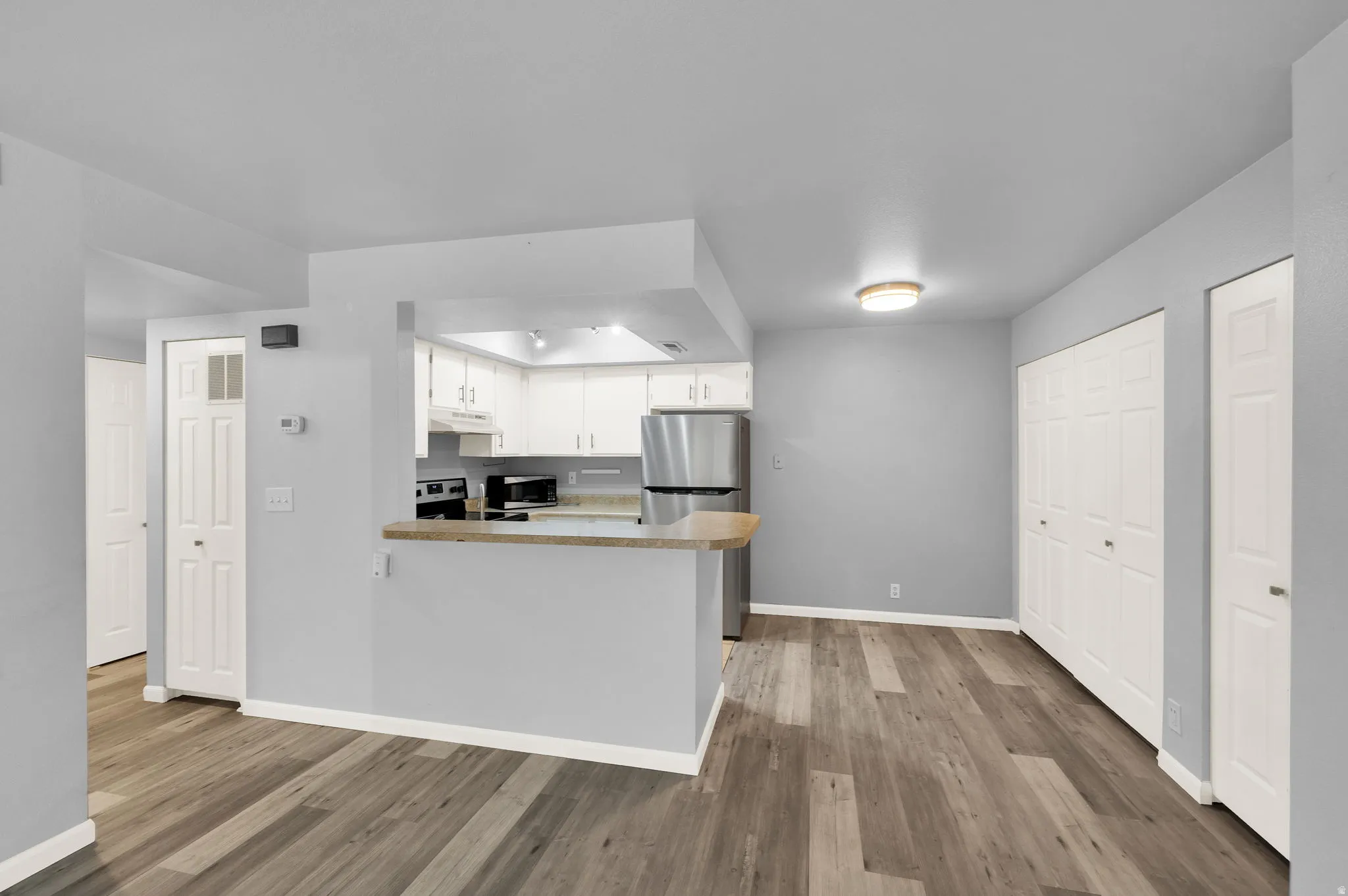 Open-concept living space featuring wood-finish flooring, a kitchen pass-through with a breakfast bar, white cabinetry, stainless steel appliances, and bi-fold closet doors