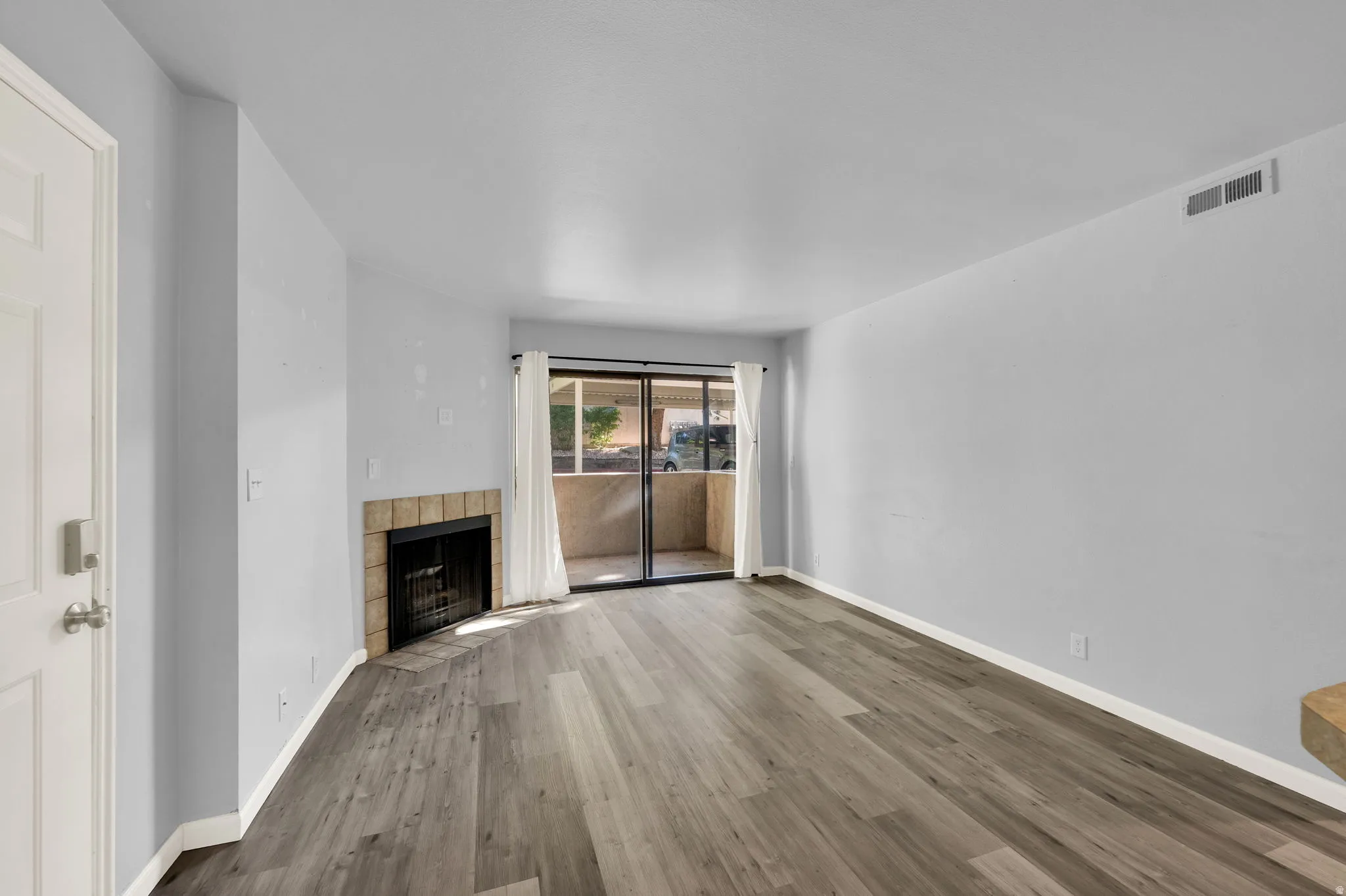 Spacious living area featuring wood-finish flooring, a tiled fireplace with hearth, and a sliding glass door to a private patio