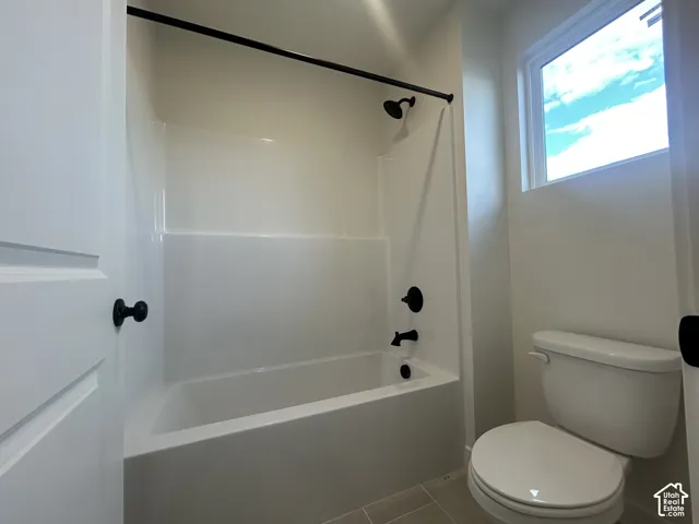 Full bathroom featuring a tub-shower combination with matte black fixtures, white surround, tile flooring, and a window