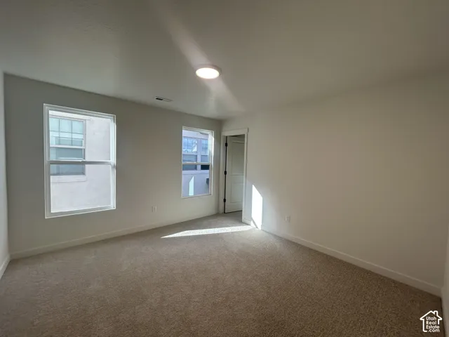 Neutral-toned interior space featuring neutral wall-to-wall carpeting, dual-pane windows with white trim, and a flush-mount overhead light fixture