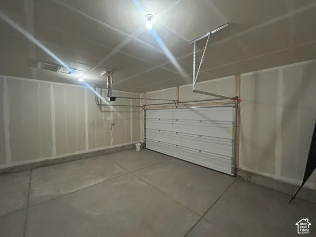 Enclosed garage featuring a concrete floor, finished drywall, and an overhead door with a motorized opener