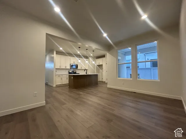 Open-concept interior featuring wood-finish flooring, recessed lighting, white cabinetry, a center kitchen island with bar seating, and large windows