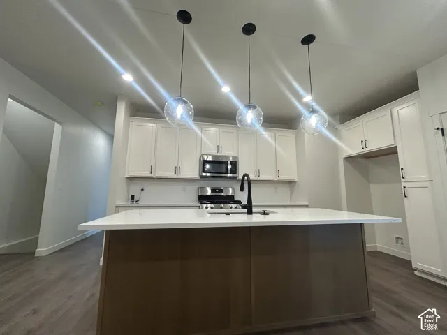 Kitchen featuring white cabinetry, a center island with a stone-finish countertop, stainless steel appliances, matte black plumbing fixtures, and three globe pendant lights
