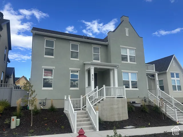 Two-story exterior featuring light green stucco siding, a steep roofline, multiple double-hung windows, and a raised entry porch with white railing