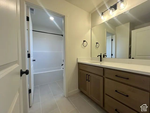 Bathroom featuring a vanity with wood-finish cabinetry, light-toned stone-style countertop, matte black hardware, integrated vanity lighting, and tiled flooring