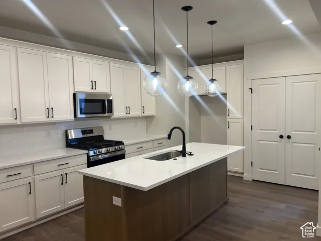 Kitchen featuring white shaker cabinetry, an island with a light-finish wood base, quartz countertops, a matte black high-arch faucet, and three spherical glass pendant lights