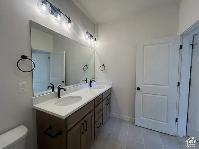 Double vanity featuring quartz countertops, undermount sinks, matte black fixtures, and wood-finish cabinetry with large-format tile flooring