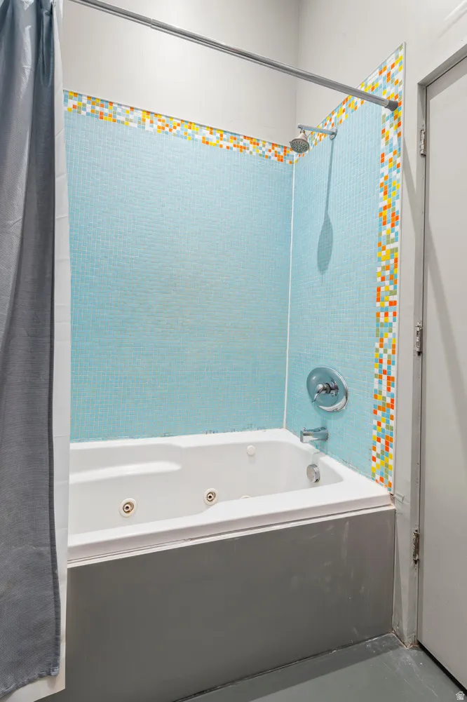 Bathroom featuring a jetted tub with shower, blue mosaic tile surround, and chrome fixtures