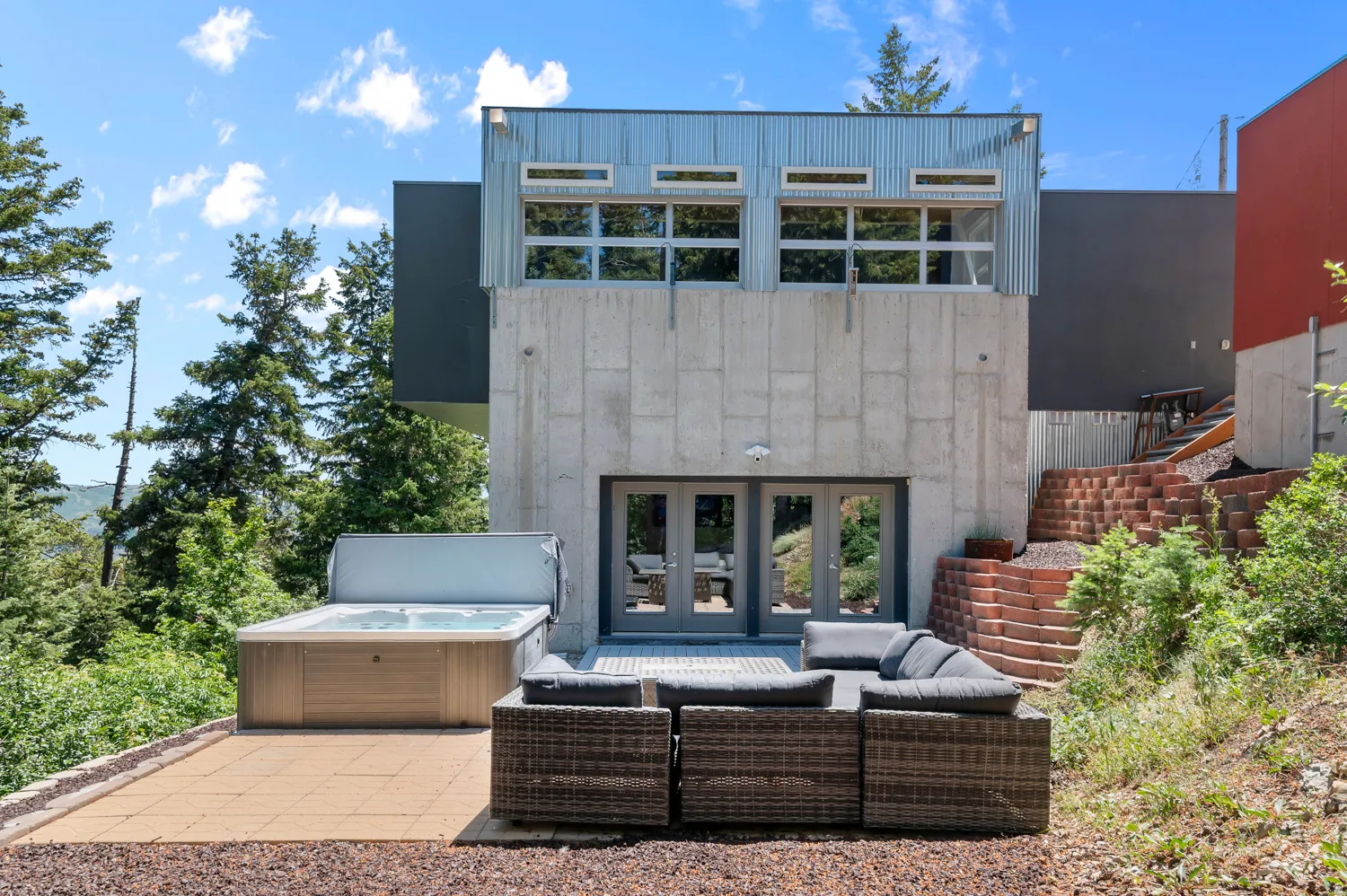 Modern exterior featuring concrete and corrugated metal siding, double glass doors, a paver patio, and terraced landscaping
