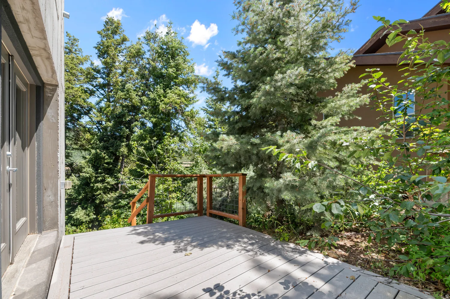 Outdoor deck featuring composite decking, wooden railings, and surrounding mature trees under a clear sky