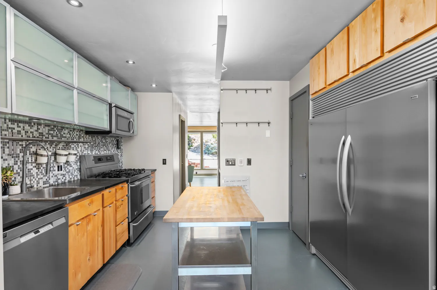 Modern kitchen featuring stainless steel appliances, mosaic tile backsplash, wood-finish lower cabinetry, and frosted-panel upper cabinets