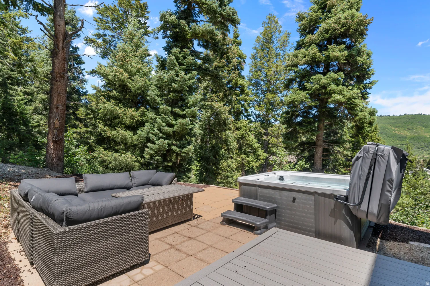 Expansive outdoor patio featuring a hot tub, tiled hardscaping, and a composite deck section