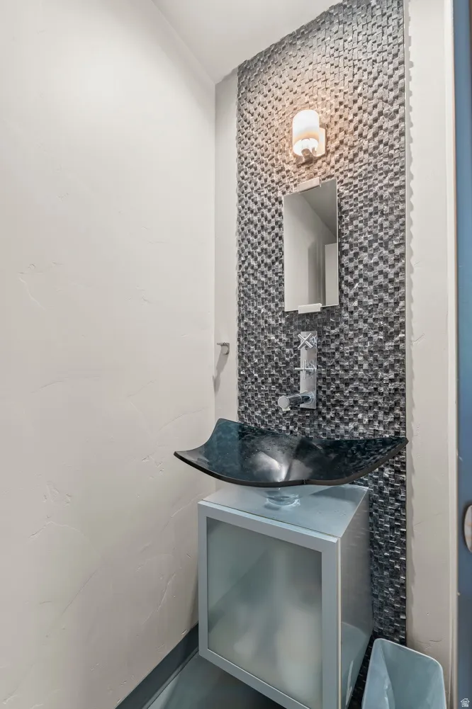 Powder room featuring a glass vessel sink, wall-mounted faucet, and a mosaic tile accent wall with a wall sconce