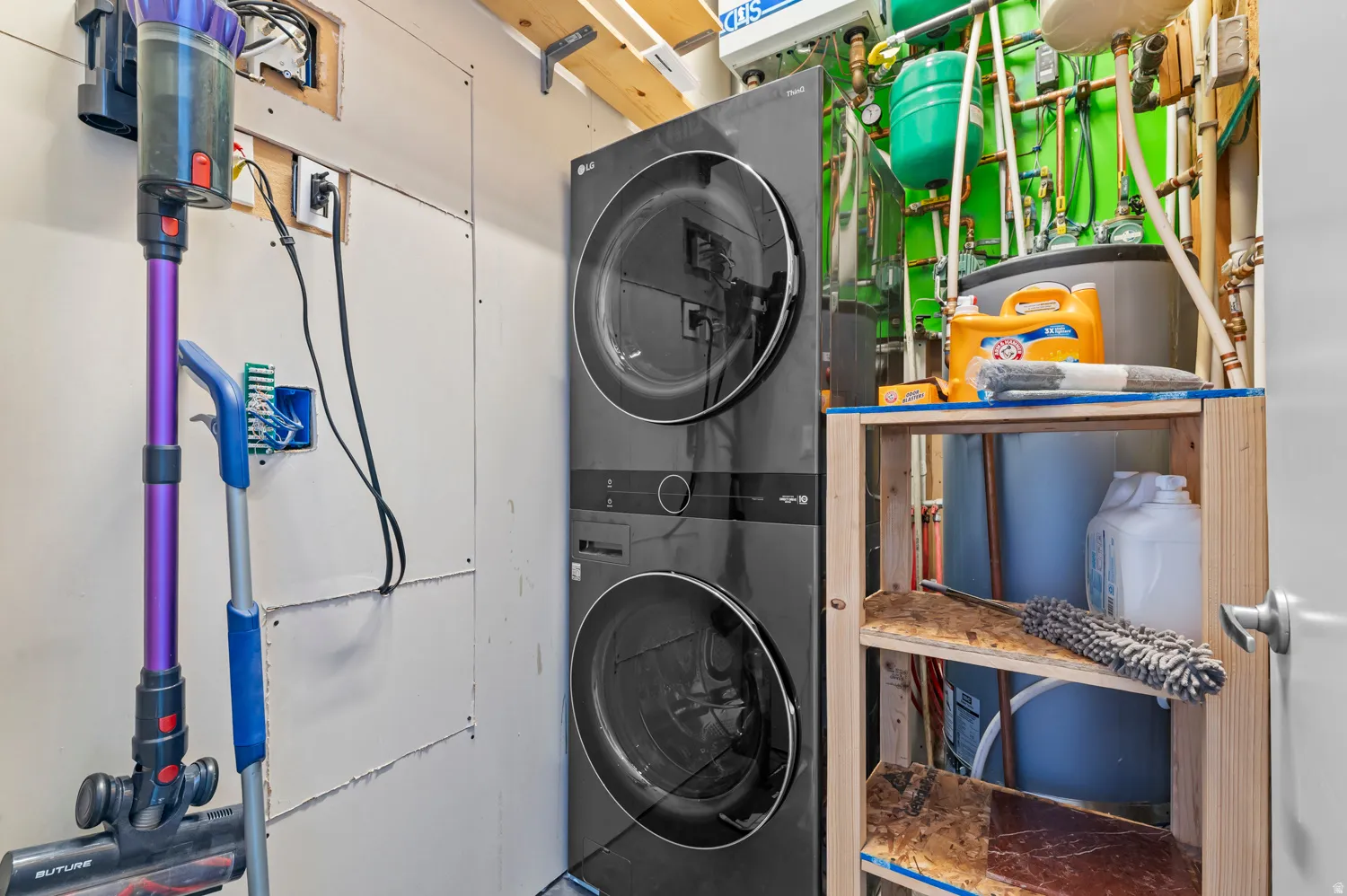 Laundry area featuring stacked washer and dryer units, exposed utility lines, and a built-in water heater