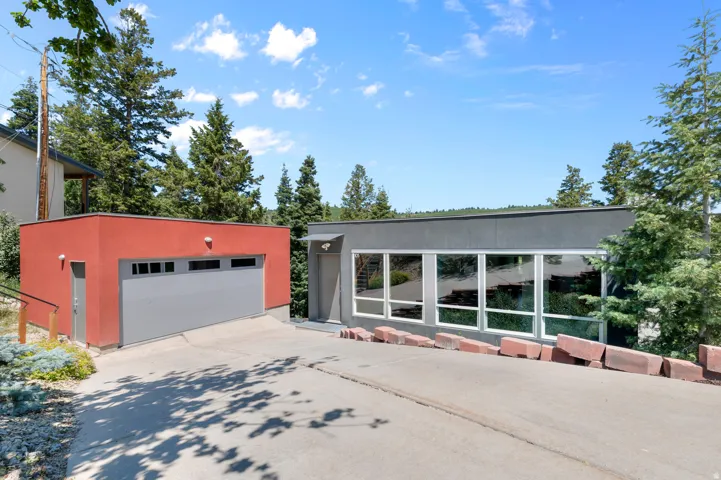 Modern exterior featuring a red detached garage with a gray garage door, a separate pedestrian door, and a gray main structure with expansive windows