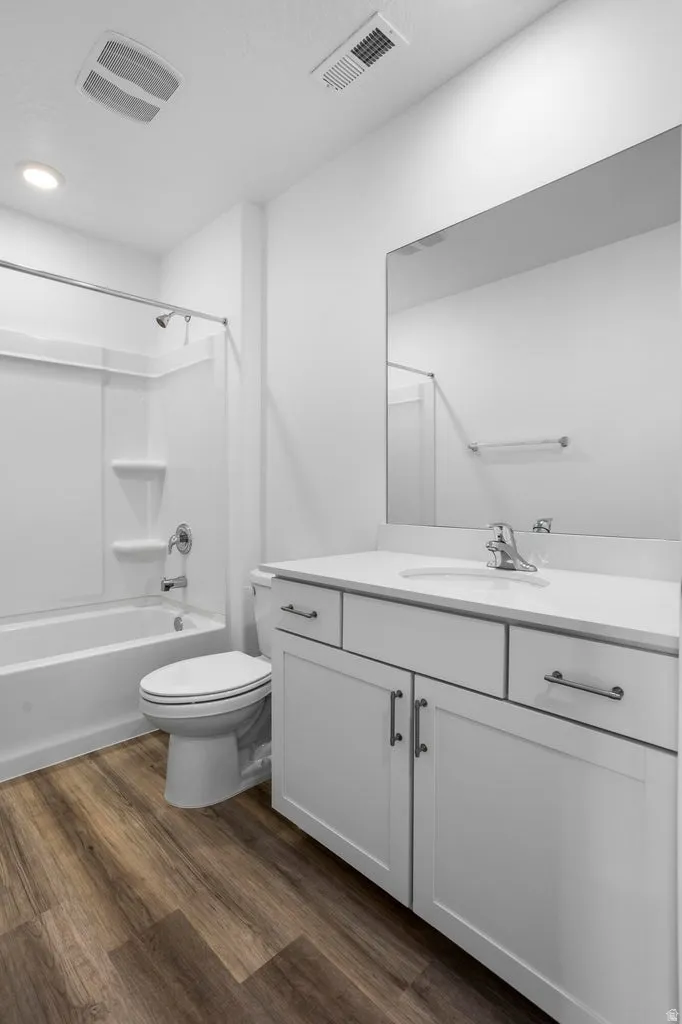 Bathroom featuring a clean white vanity with a single basin sink, white cabinetry with hardware, a full-width wall mirror, wood-finish flooring, and a bathtub with shower