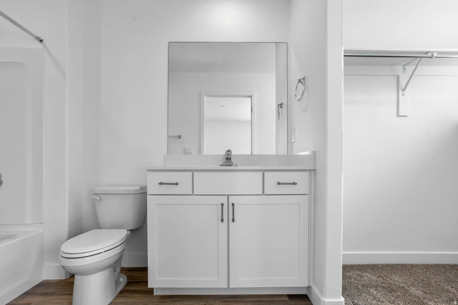 Bathroom featuring a white vanity with two drawers and two cabinet doors, a rectangular vanity mirror, a standard toilet, and a white bathtub with an integrated shower
