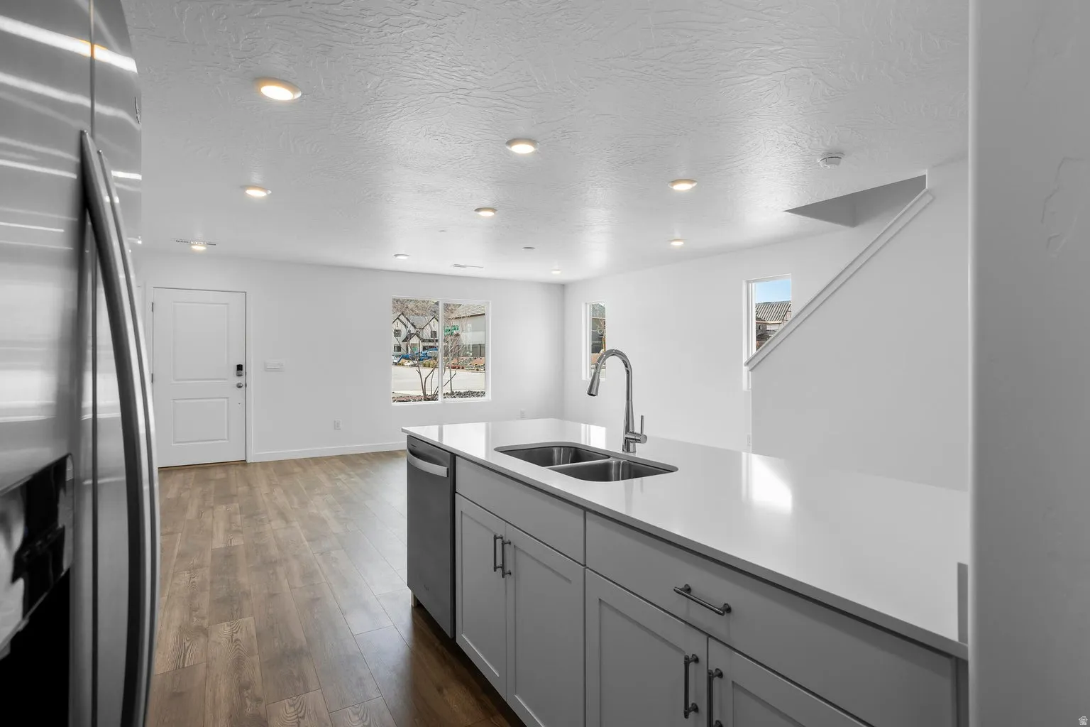 Kitchen island featuring a double basin sink with a gooseneck faucet, light-toned countertops, and gray shaker-style cabinetry with dark hardware