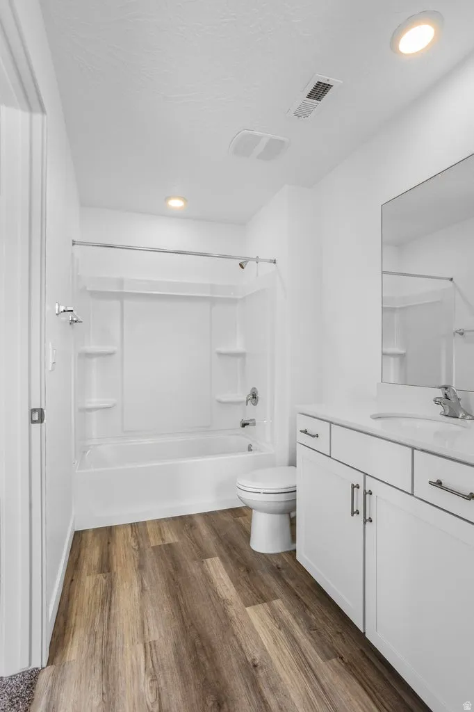 Full bathroom featuring a white tub/shower combination, wood-finish flooring, a white vanity with integrated sink, and recessed lighting
