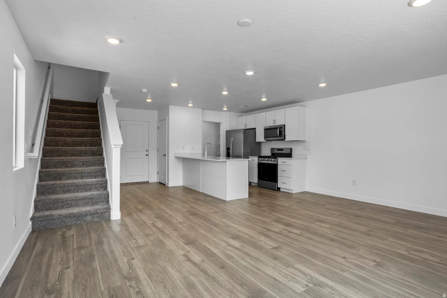 Open-concept living area featuring wood-finish flooring, recessed lighting, a white kitchen island with counter seating, white cabinetry, and stainless steel appliances