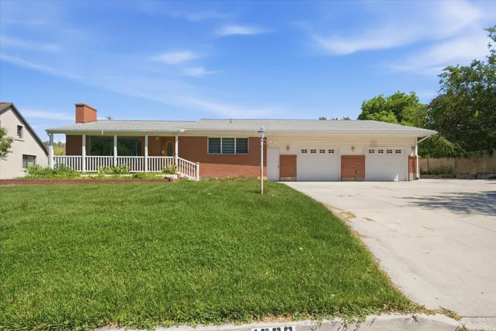 Single-story brick residence featuring a covered porch with white railing, a three-car attached garage, and a concrete driveway