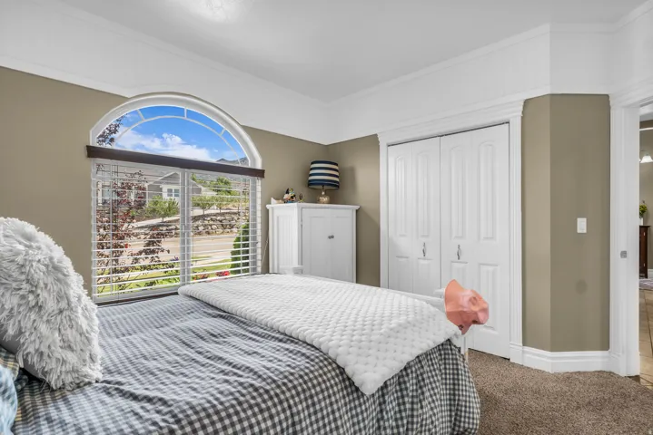 Room featuring an arched window with louvered blinds, crown molding, bifold closet doors, and carpet flooring