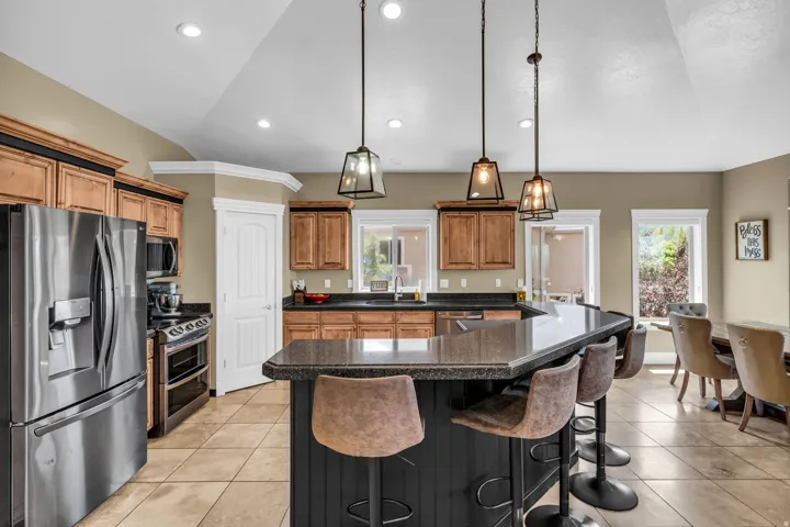 Kitchen featuring a dark-toned breakfast bar, pendant lighting, stainless steel appliances, light wood-finish cabinetry, and tile flooring