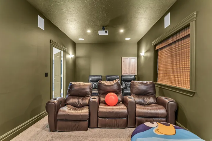 Dedicated media room featuring recessed lighting, wall sconces, integrated ceiling speakers, and a ceiling-mounted projector