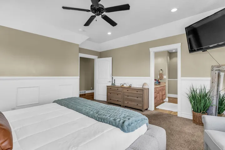 Carpeted bedroom featuring wainscoting, a tray ceiling, and a ceiling fan with integrated lighting