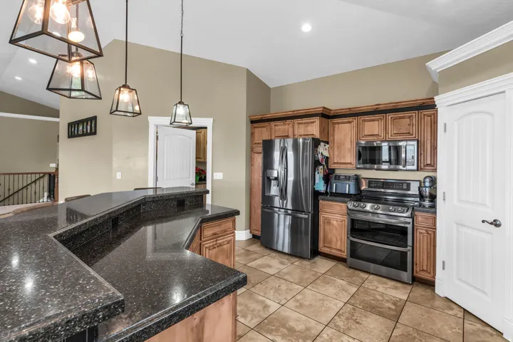 Kitchen featuring a multi-level breakfast bar with speckled countertops, wood-finish cabinetry, stainless steel appliances, and recessed lighting