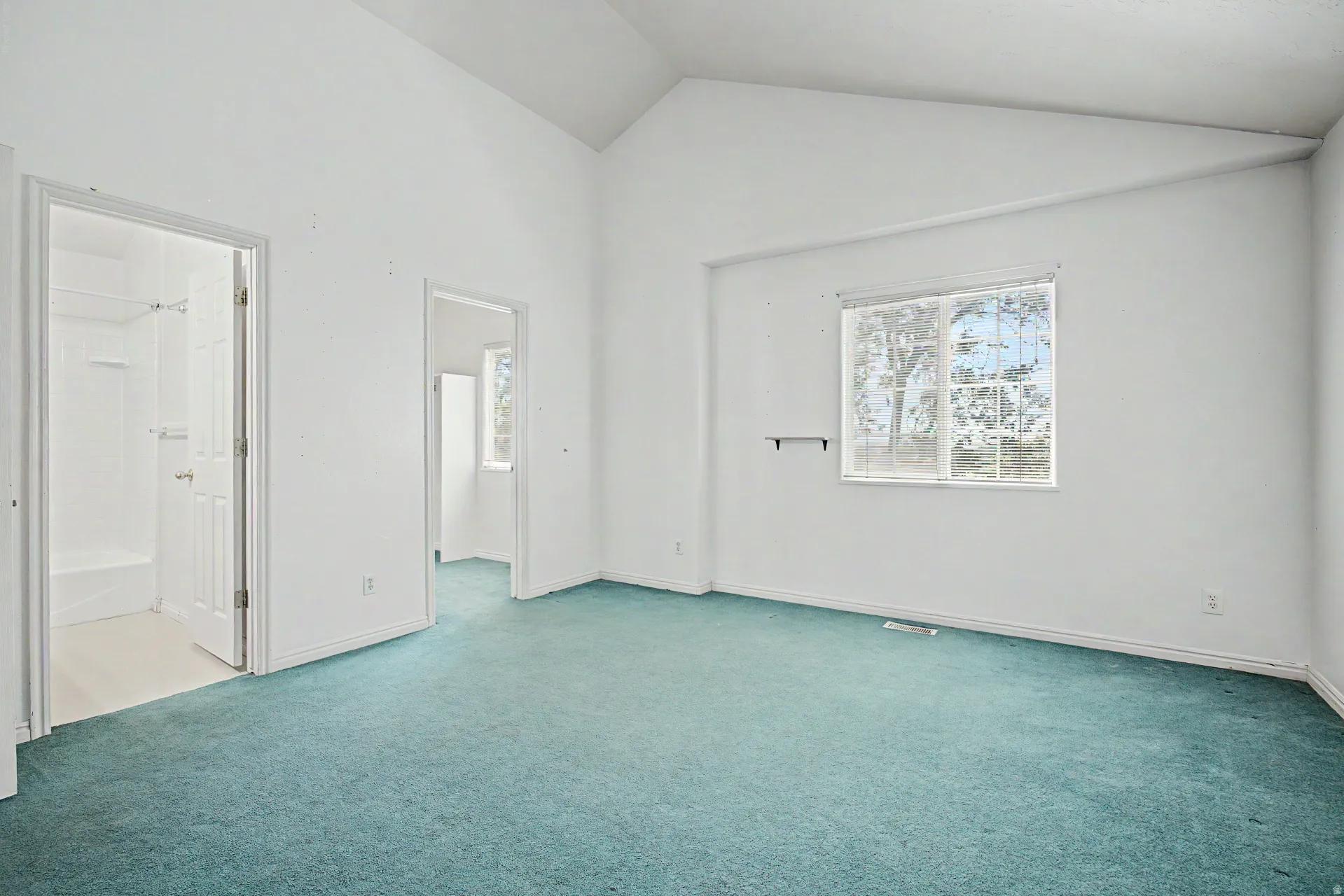 Bright room featuring vaulted ceilings, a large window, teal carpeting, and white painted walls