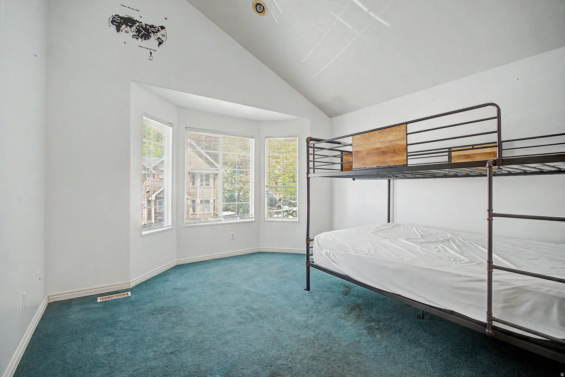 Room featuring vaulted ceilings, a bay window with multiple panes, white wall finishes, and blue carpet flooring