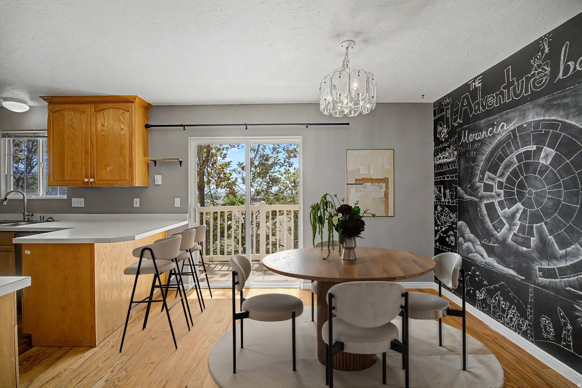 Virtually staged Kitchen and dining area featuring light wood-finish flooring, a white countertop island with seating, natural wood cabinetry, and a black chalkboard wall