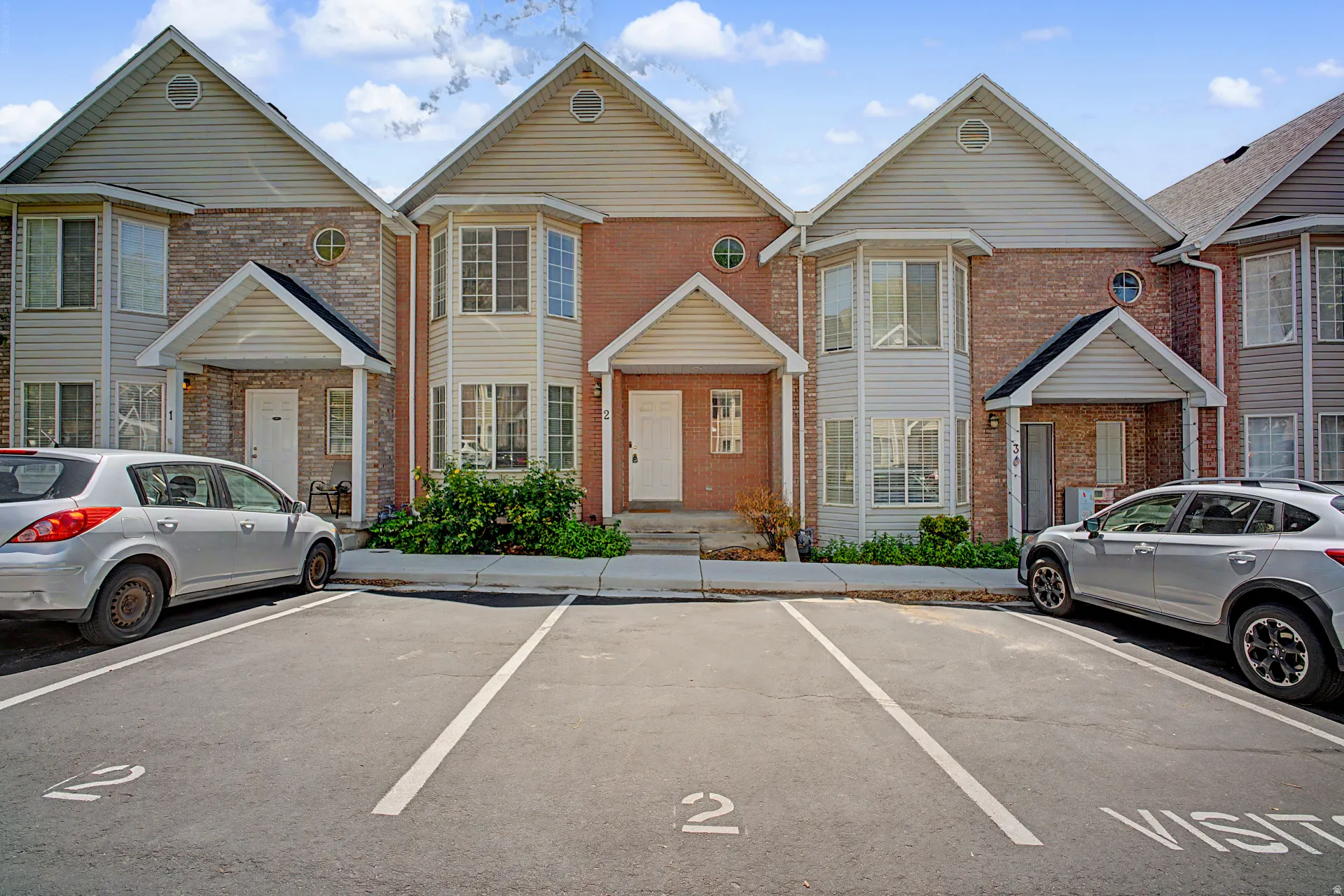 Townhome exterior featuring brick and siding facade, bay windows, gabled rooflines, and covered entryways