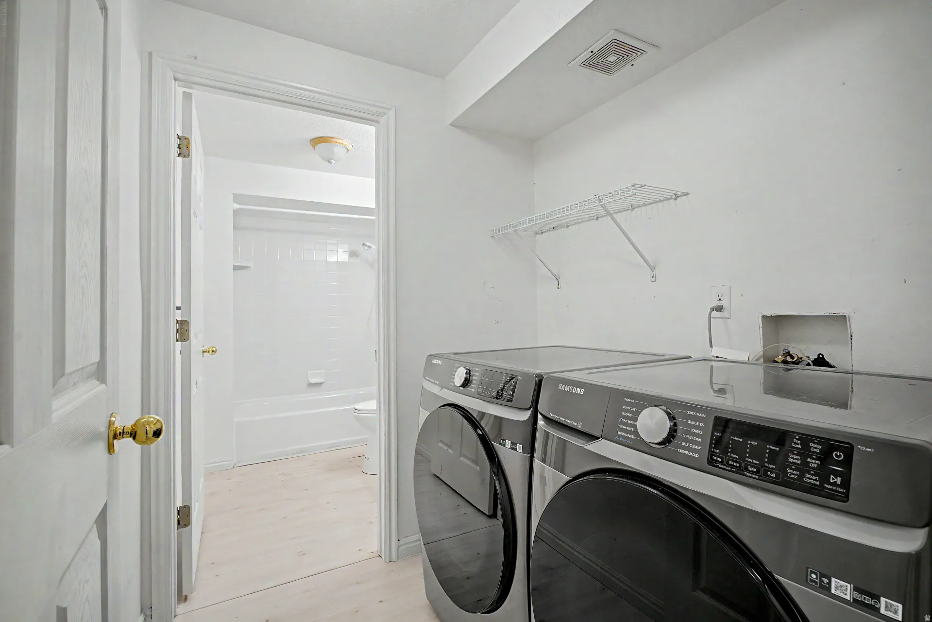 Dedicated laundry area featuring front-loading machines, overhead wire shelving, and light-toned flooring
