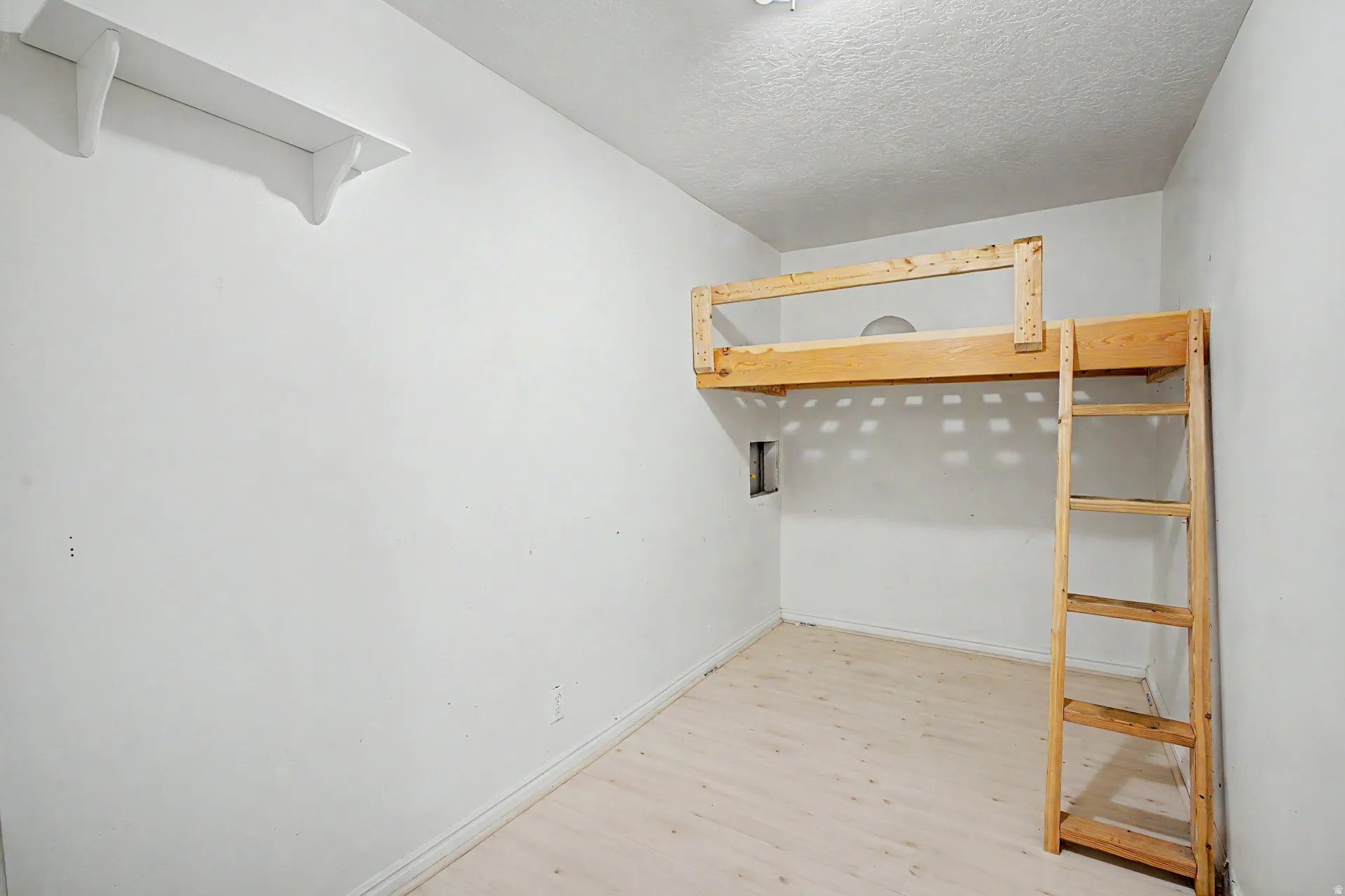 Room featuring a built-in wooden loft bed with ladder, light-toned wood-finish flooring, and white walls