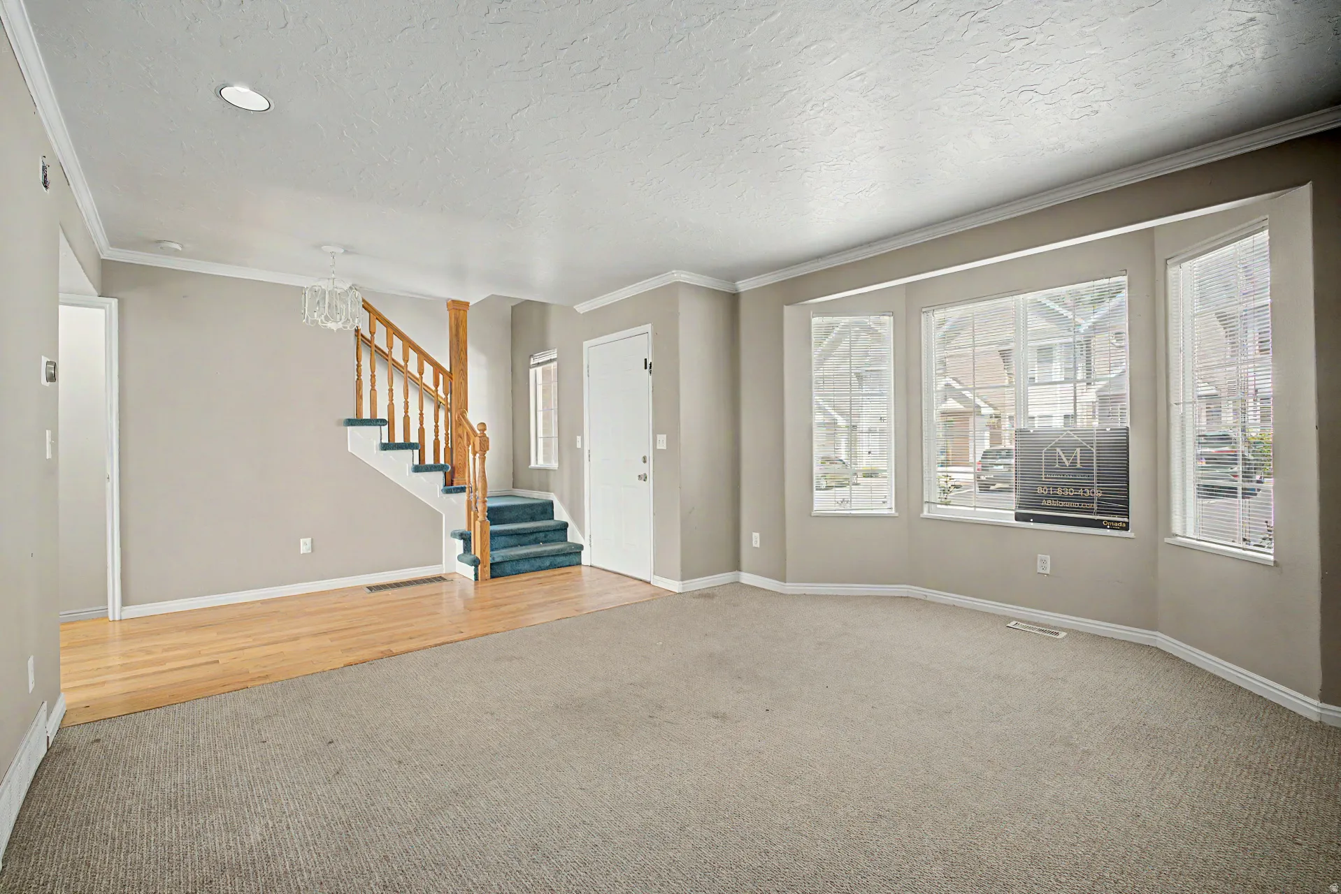 Spacious living area featuring a bay window, crown molding, and a combination of wood-finish flooring and carpeting