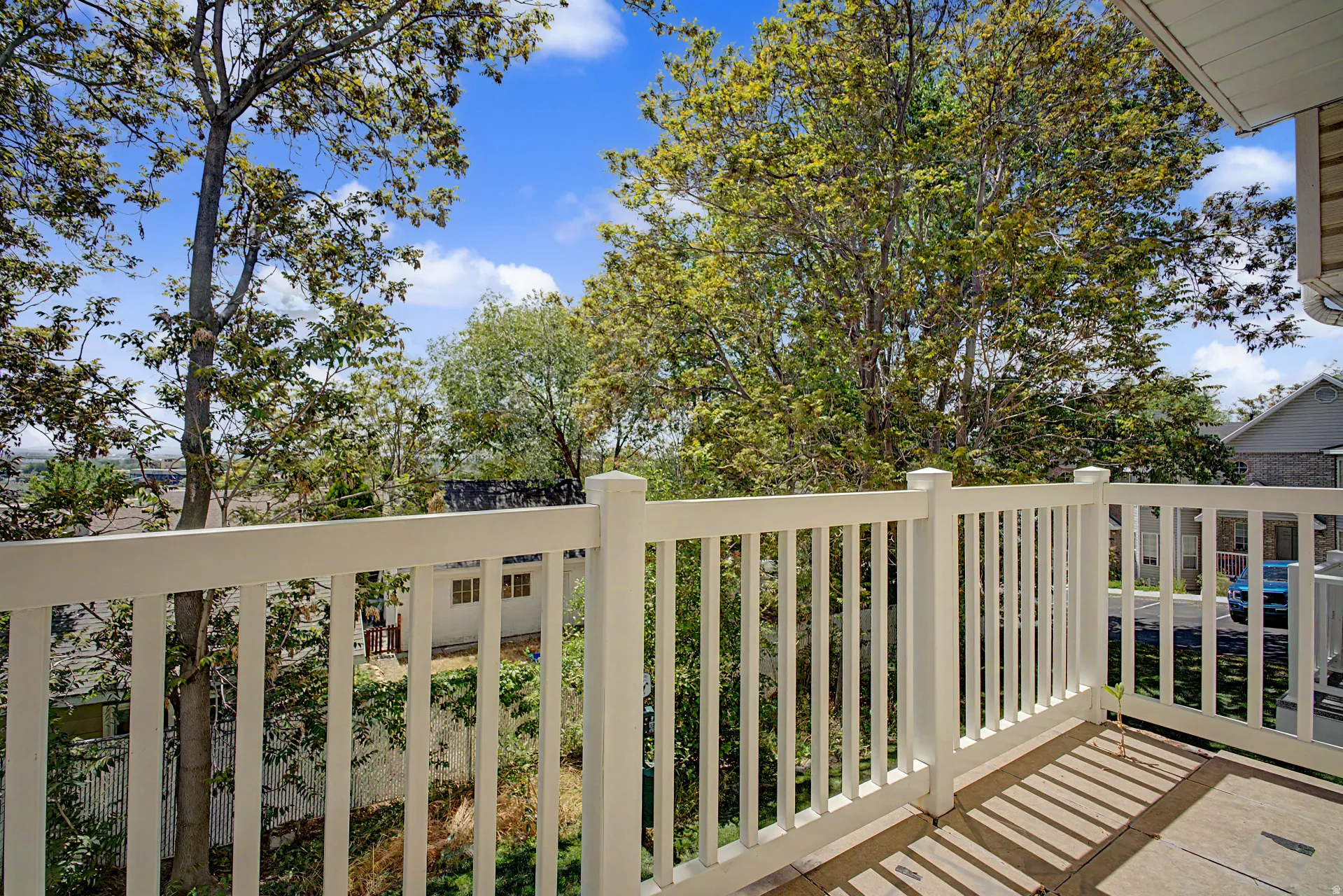 Outdoor balcony featuring white railing, concrete flooring, and mature trees providing natural screening