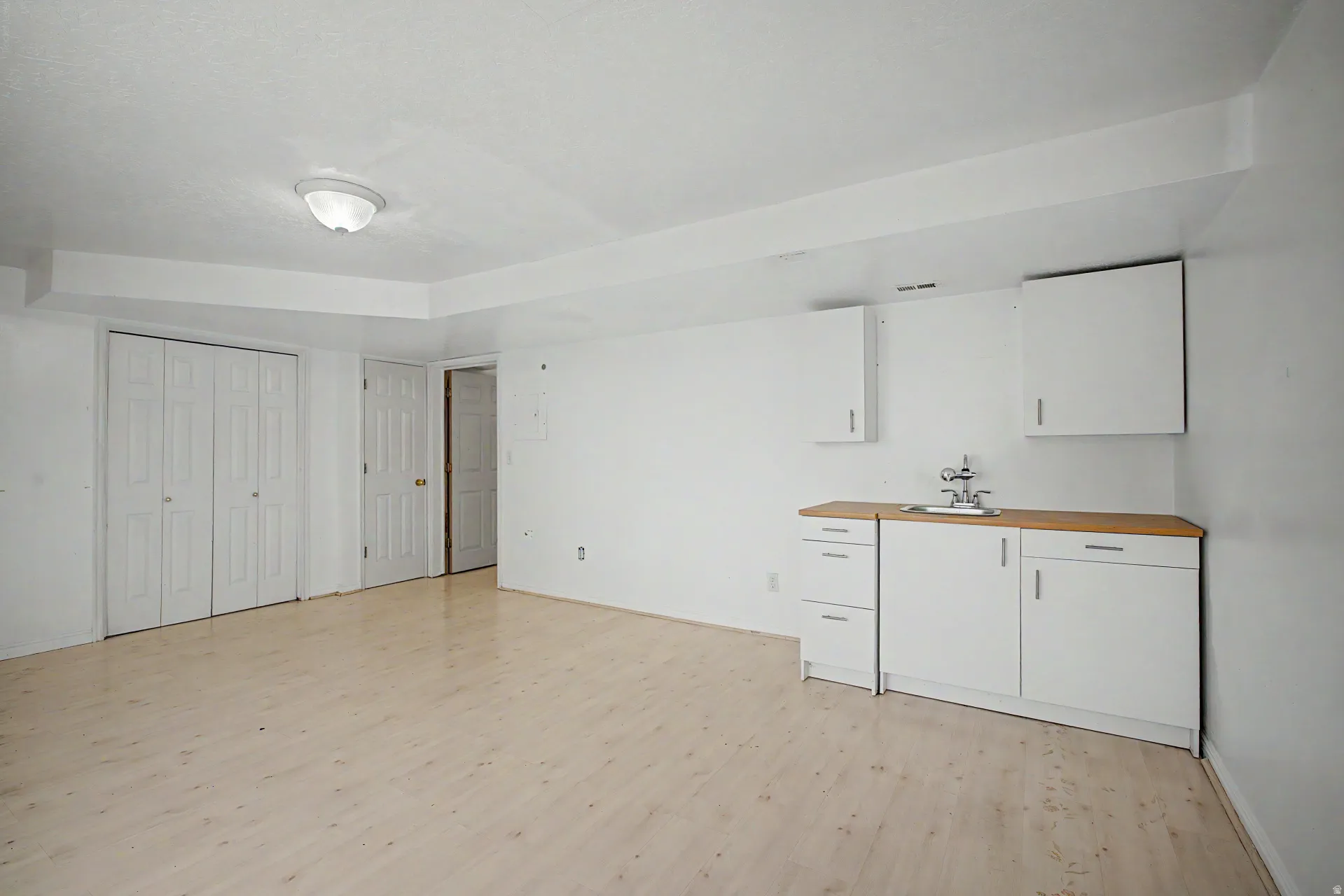 Open space featuring wood-finish flooring, a functional wet bar with wood-finish countertop, and white cabinetry