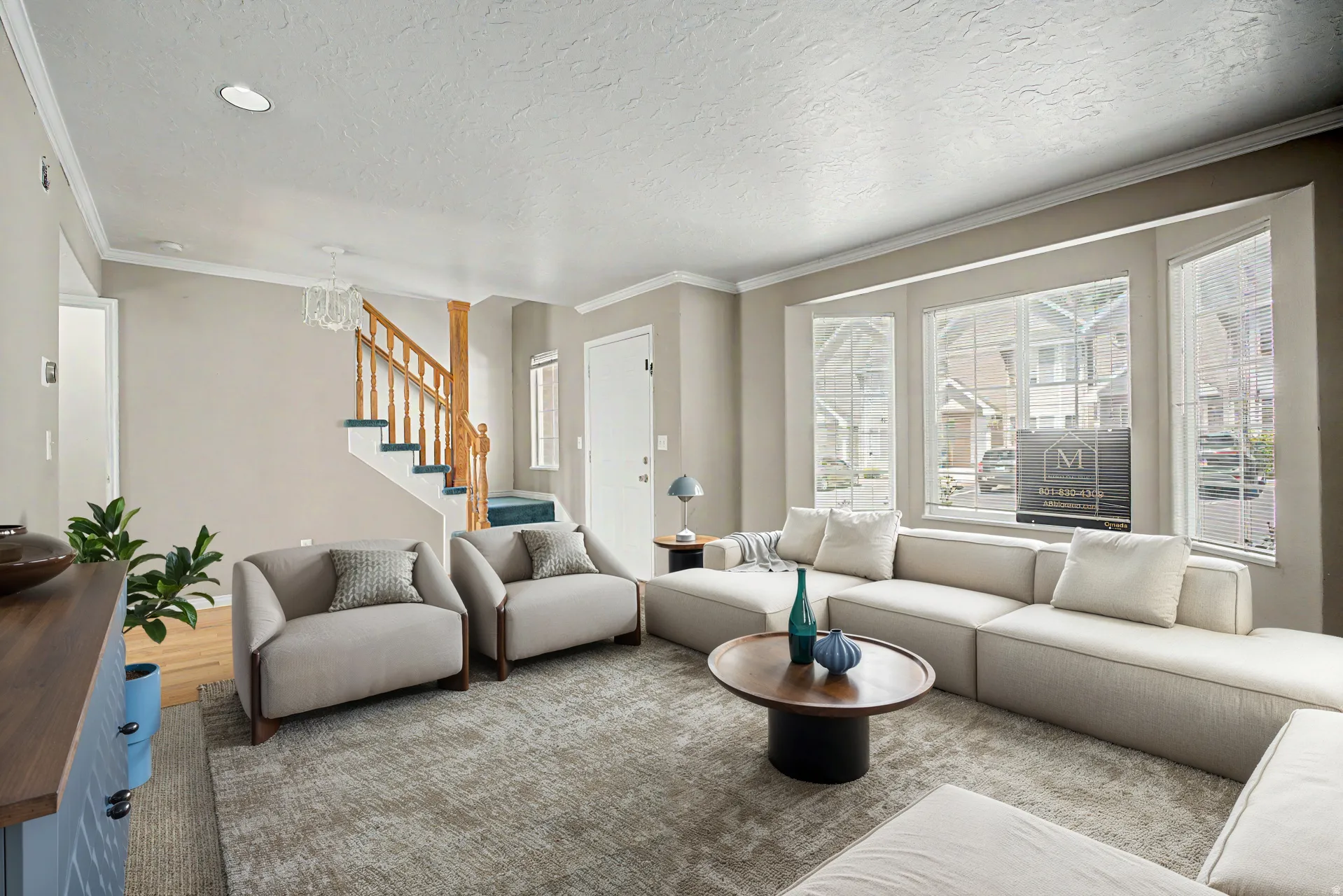 Virtually staged Living area featuring a bay window, crown molding, light wood-finish flooring, and a stairway with wood newel posts and handrails