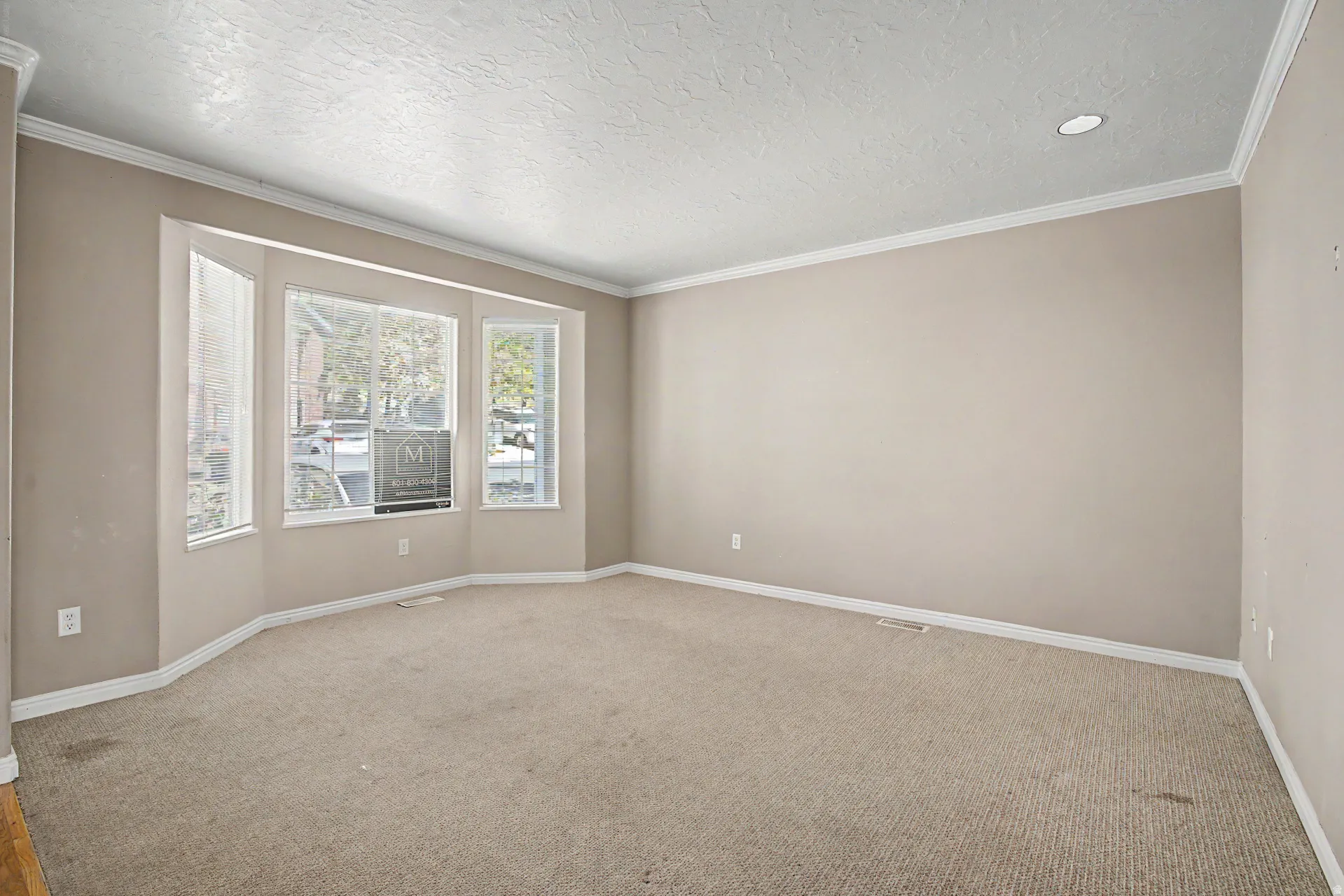 Spacious room featuring a bay window, neutral carpeting, recessed lighting, and crown molding