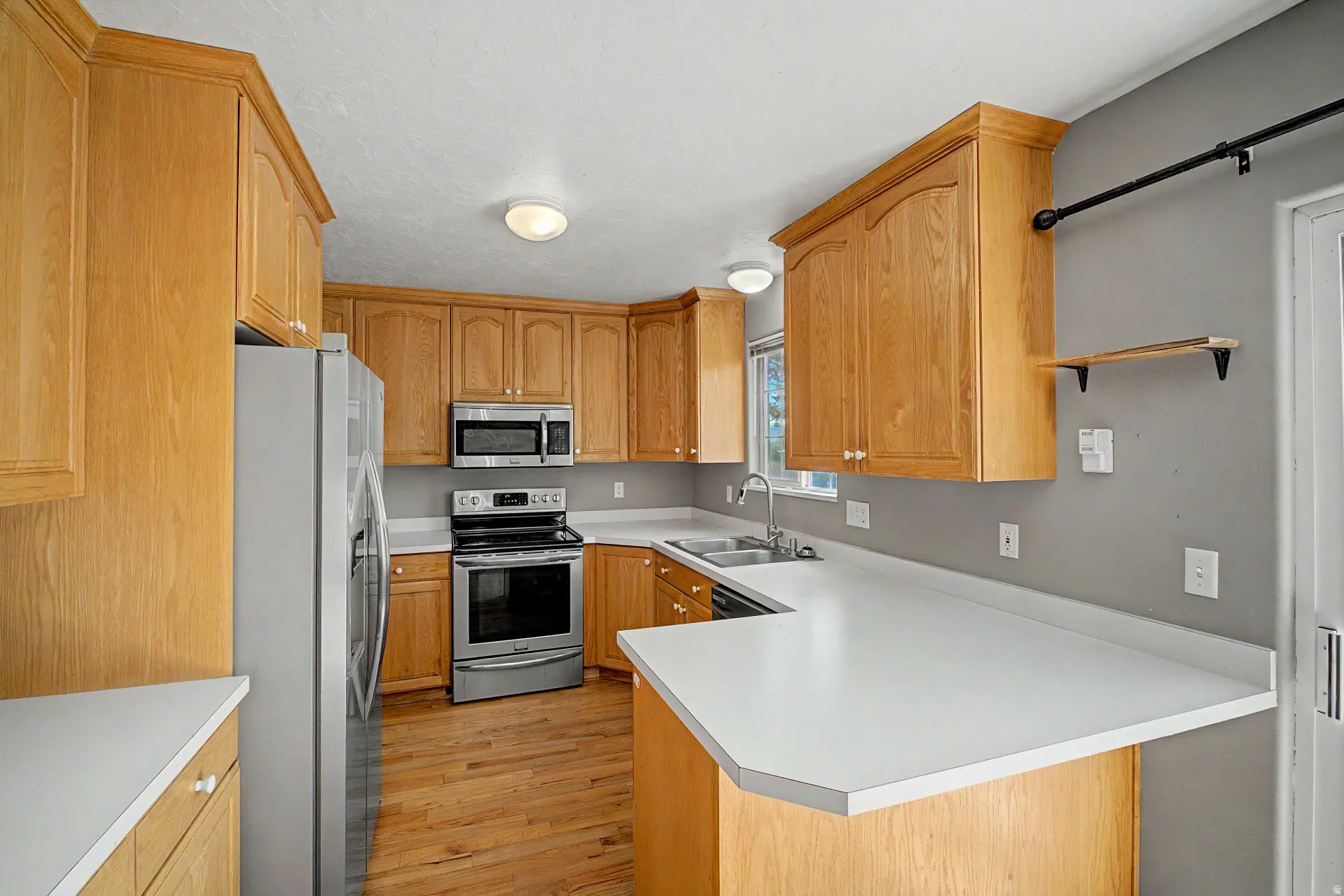 Kitchen featuring light wood cabinetry, stainless steel appliances, solid surface countertops, a double basin sink, and wood-finish flooring
