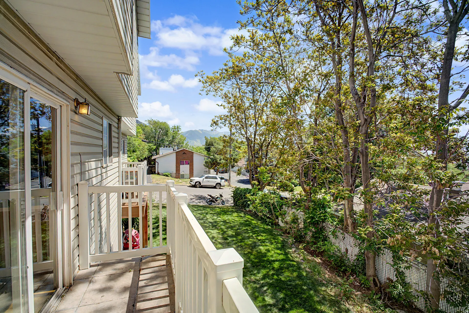 Private balcony with a sliding glass door, white railing, and exterior wall light