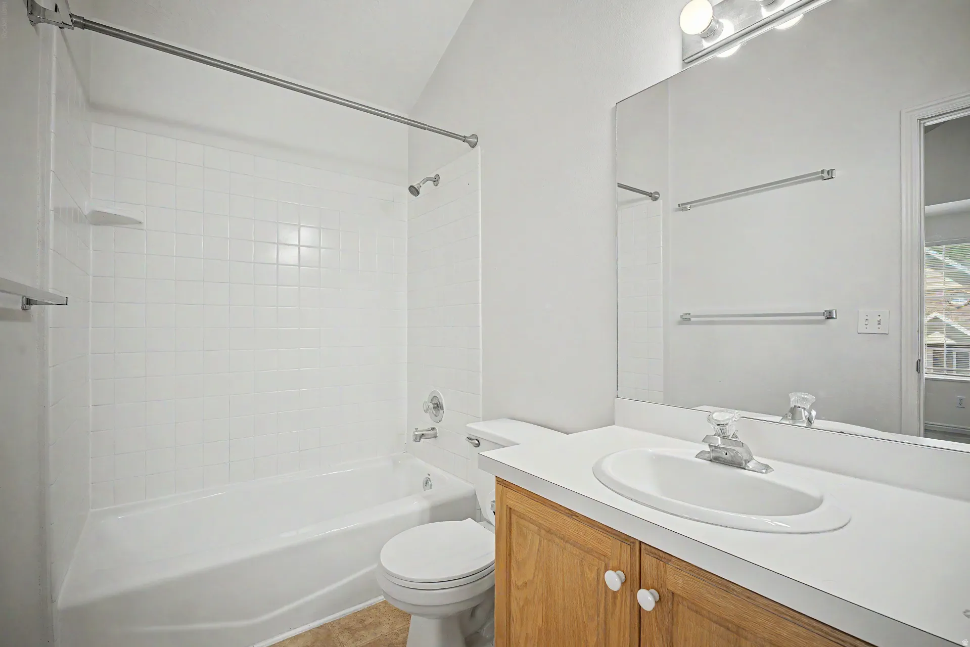 Full bathroom featuring a white tile shower surround, a white bathtub, and a light wood-finish vanity with a white countertop and integrated sink