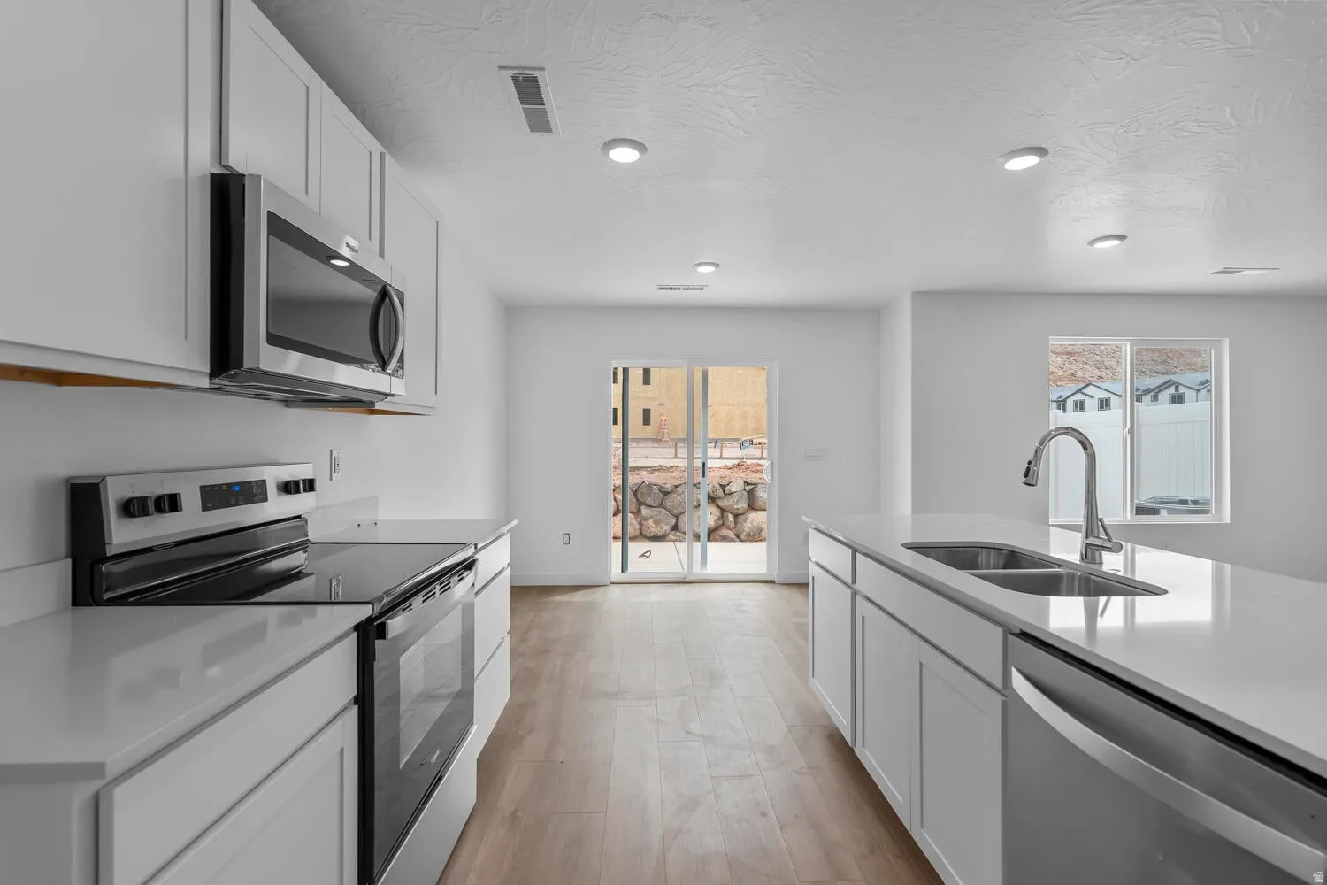 Modern kitchen featuring white cabinetry, stainless steel appliances, wood-finish flooring, recessed lighting, and a kitchen island with an integrated sink